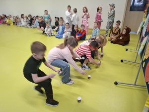 Dzieci w strojach karnawałowych siedzą i uczestniczą w zabawie ruchowej na podłodze sali teatralnej.