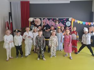 Duża grupa uczniów klas 0–III w różnorodnych przebraniach karnawałowych siedzi i klęczy do wspólnego zdjęcia na sali teatralnej.