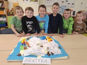 Grupa dzieci stoi za stołem z makietą Arktyki; na makiecie widoczne są lód, zwierzęta polarne i klocki.