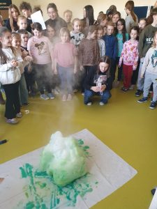 Uczeń klasy 7 l przeprowadza eksperyment chemiczny powodujący intensywne pienienie się substancji, obserwowany przez uczniów klas 0–3.