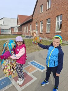 Dziewczynka i chłopiec trzymają kukły wykonane z materiałów plastycznych podczas pożegnania zimy.