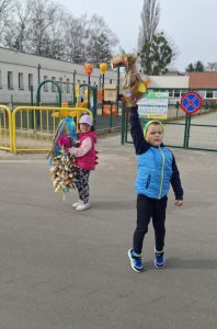 Chłopiec trzyma kukłę symbolizującą zimę podczas szkolnego wydarzenia na świeżym powietrzu.