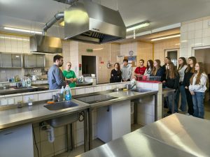 Ósmoklasiści w pracowni gastronomicznej podczas prezentacji wyposażenia i zajęć praktycznych.