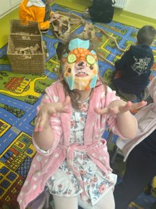 Dziewczynka siedzi w klasie z maseczką na twarzy i plasterkami ogórka na oczach podczas zabawy spa z okazji Dnia Kobiet.