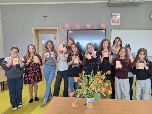 Uczennice stoją w klasie i prezentują otrzymane upominki z okazji Dnia Kobiet.