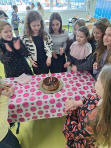 Uczennice stoją wokół stołu z tortem przygotowanym na szkolne obchody Dnia Kobiet.