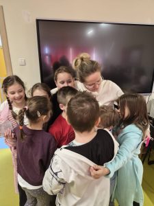 Uczniowie przytulają nauczycielkę podczas wspólnego świętowania Dnia Kobiet w klasie.