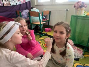 Uczennice wykonują makijaż koleżance podczas szkolnej zabawy spa z okazji Dnia Kobiet.