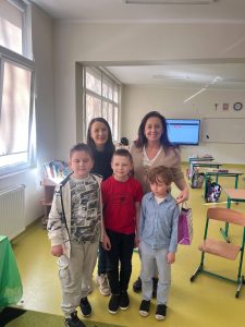 Nauczycielki i uczniowie stoją razem w klasie podczas szkolnych obchodów Dnia Kobiet.