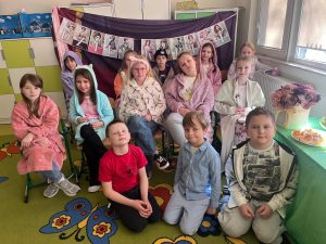 Grupa uczniów siedzi w klasie przed dekoracją z napisem „Dzień Kobiet” podczas szkolnych obchodów.