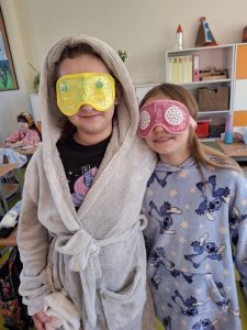 Dwie uczennice w szlafrokach stoją w klasie w kolorowych opaskach na oczy podczas szkolnego dnia spa.