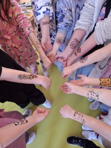 Uczniowie prezentują tymczasowe tatuaże wykonane na przedramionach podczas szkolnych obchodów Dnia Kobiet.