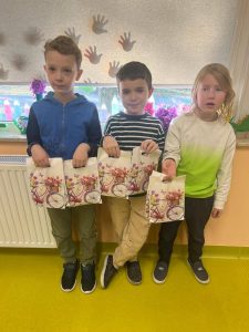 Trójka uczniów trzyma ozdobne torebki z upominkami przygotowanymi z okazji Dnia Kobiet.