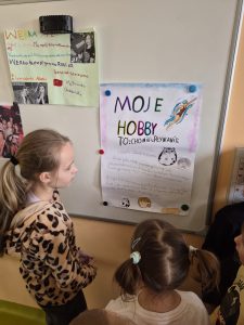 Uczniowie klas 1–3 oglądają plakat zatytułowany „Moje hobby”, przedstawiający zainteresowania związane z hodowlą chomików i pływaniem.
