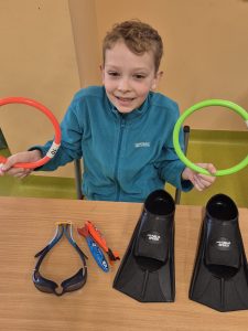 Uczeń klas 1–3 siedzi przy stoliku i pokazuje akcesoria sportowe jako swoje hobby związane z aktywnością fizyczną.