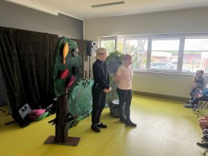 Aktorzy stoją na scenie obok dekoracji przedstawiającej drzewo i leśną scenografię.