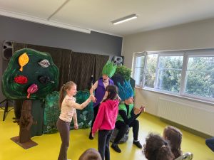 Aktorzy w kostiumach Trolli rozmawiają z dziećmi biorącymi udział w scenie podczas przedstawienia teatralnego.