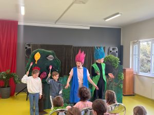 Aktorzy prowadzą przedstawienie, a dzieci stoją na scenie i trzymają rekwizyty w kształcie liści.