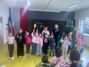 Dzieci i aktorzy stoją razem na scenie po zakończeniu przedstawienia i trzymają teatralne rekwizyty.