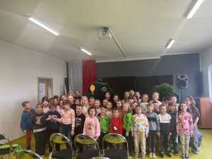Duża grupa uczniów stoi do wspólnego zdjęcia po przedstawieniu teatralnym w szkolnej sali.