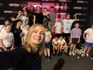 Grupowe zdjęcie uczniów z nauczycielem wykonane na tle ścianki klubu Interpadel, dzieci pozują i uśmiechają się do aparatu.