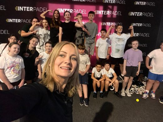 Grupowe zdjęcie uczniów z nauczycielem wykonane na tle ścianki klubu Interpadel, dzieci pozują i uśmiechają się do aparatu.