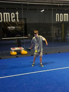 Uczeń odbija piłkę rakietą do padla na korcie, ćwicząc podstawowe umiejętności.