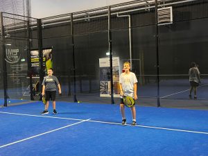 Dwóch uczniów stoi na korcie, trzymając rakiety i przygotowując się do kolejnej wymiany piłki.