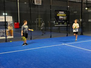 Dwóch uczniów stoi naprzeciw siebie na niebieskim korcie do padla, przygotowując się do gry.