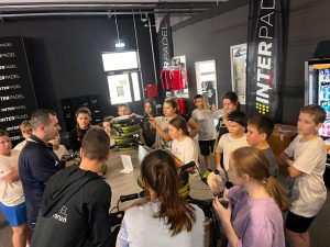 Grupa uczniów zgromadzona wokół instruktora słucha wyjaśnień dotyczących zasad gry i sprzętu do padla.