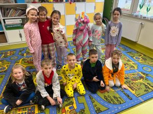 Dzieci w piżamach siedzą i klęczą na kolorowym dywanie w sali lekcyjnej podczas Dnia w Piżamie.