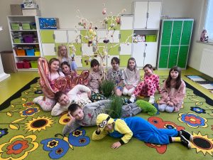Grupa dzieci w piżamach odpoczywa na dywanie w sali, świętując wspólnie szkolny Dzień w Piżamie z okazji Pierwszego Dnia Wiosny.