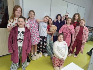 Grupa uczennic w kolorowych piżamach pozuje w sali lekcyjnej podczas szkolnego Dnia w Piżamie.