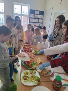 Uczniowie ustawiają się przy stole z kanapkami i warzywami, przygotowanymi na szkolny Dzień w Piżamie.