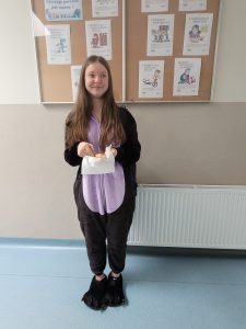 Uczennica w stroju piżamowym stoi na korytarzu i trzyma przekąskę podczas szkolnych obchodów Dnia w Piżamie.