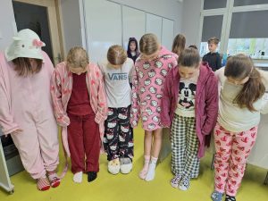 Uczniowie stoją w rzędzie w szkolnej sali i patrzą na swoje stopy w kolorowych, niepasujących skarpetkach – gest solidarności ze Światowym Dniem Downa.