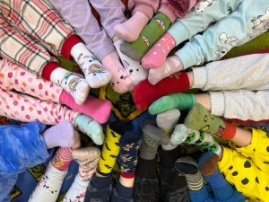 Dzieci siedzą w kręgu i wyciągają stopy w kolorowych, niepasujących skarpetkach, okazując wsparcie dla osób z zespołem Downa.