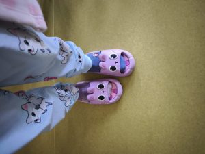 Zbliżenie na stopy w dwóch różnych skarpetkach w różowych klapkach z uszami i dużymi oczami – symbol wsparcia dla Światowego Dnia Downa.