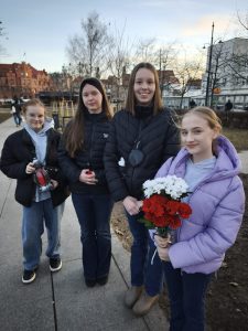Cztery uczennice Samorządu Uczniowskiego stoją z kwiatami i zniczem po złożeniu hołdu przy pomniku Ofiar Wyklętych 1 marca.