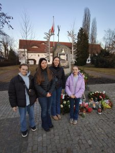Uczennice Samorządu Uczniowskiego stoją przy pomniku Ofiar Wyklętych po złożeniu kwiatów i zapaleniu zniczy w dniu 1 marca.