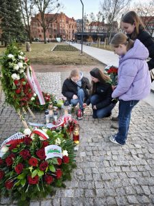 Uczennice Samorządu Uczniowskiego zapalają znicze i składają kwiaty przy pomniku Ofiar Wyklętych podczas obchodów 1 marca.