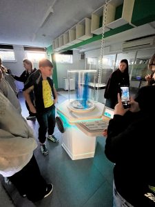 Uczniowie obserwują doświadczenie z wirującą cieczą w cylindrycznym urządzeniu demonstracyjnym.