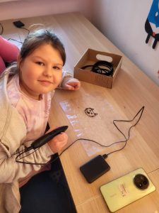 Uczennica tworzy rysunek przy użyciu długopisu 3D podczas warsztatów.