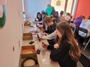 Uczniowie pracują przy stanowiskach warsztatowych, korzystając z długopisów 3D.