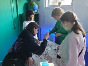 Uczniowie pod opieką nauczyciela budują obwody elektryczne na interaktywnym stanowisku edukacyjnym.