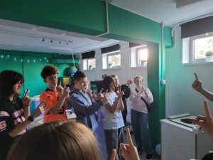 Grupa uczniów wykonuje doświadczenie z podniesionymi palcami podczas zajęć edukacyjnych w laboratorium. Celem jego jest pokazanie przesunięcia się obrazu w zależności od patrzącego oka.