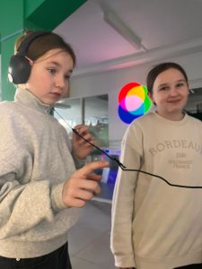 Uczennica słucha przez słuchawki dźwięków kosmosu, obok stoi druga uczennica.