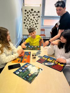 Grupa uczniów bierze udział w edukacyjnej grze planszowej o tematyce kosmicznej pod opieką prowadzącego.