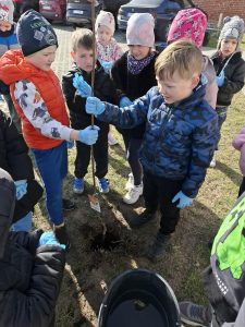 Dzieci trzymają i ustawiają sadzonkę drzewa przed zasadzeniem w ziemi.