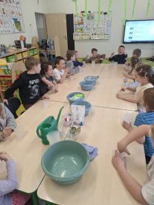 Dzieci siedzą przy stole i uczestniczą w prostych eksperymentach związanych z wodą i środowiskiem.